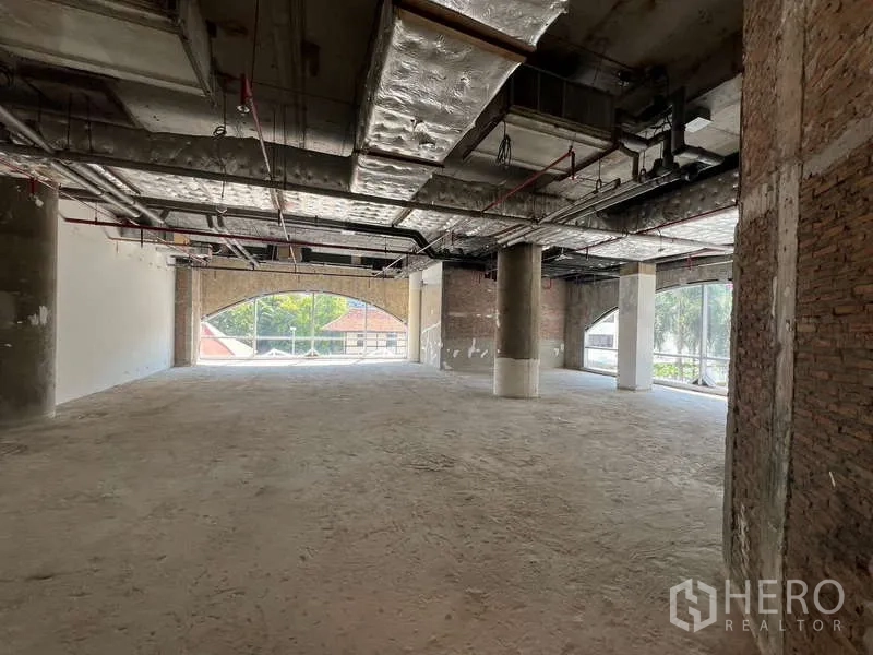 Retail Space for rent - Shell retail interior with exposed ductwork ceiling, concrete floor and large arched windows bringing natural light.