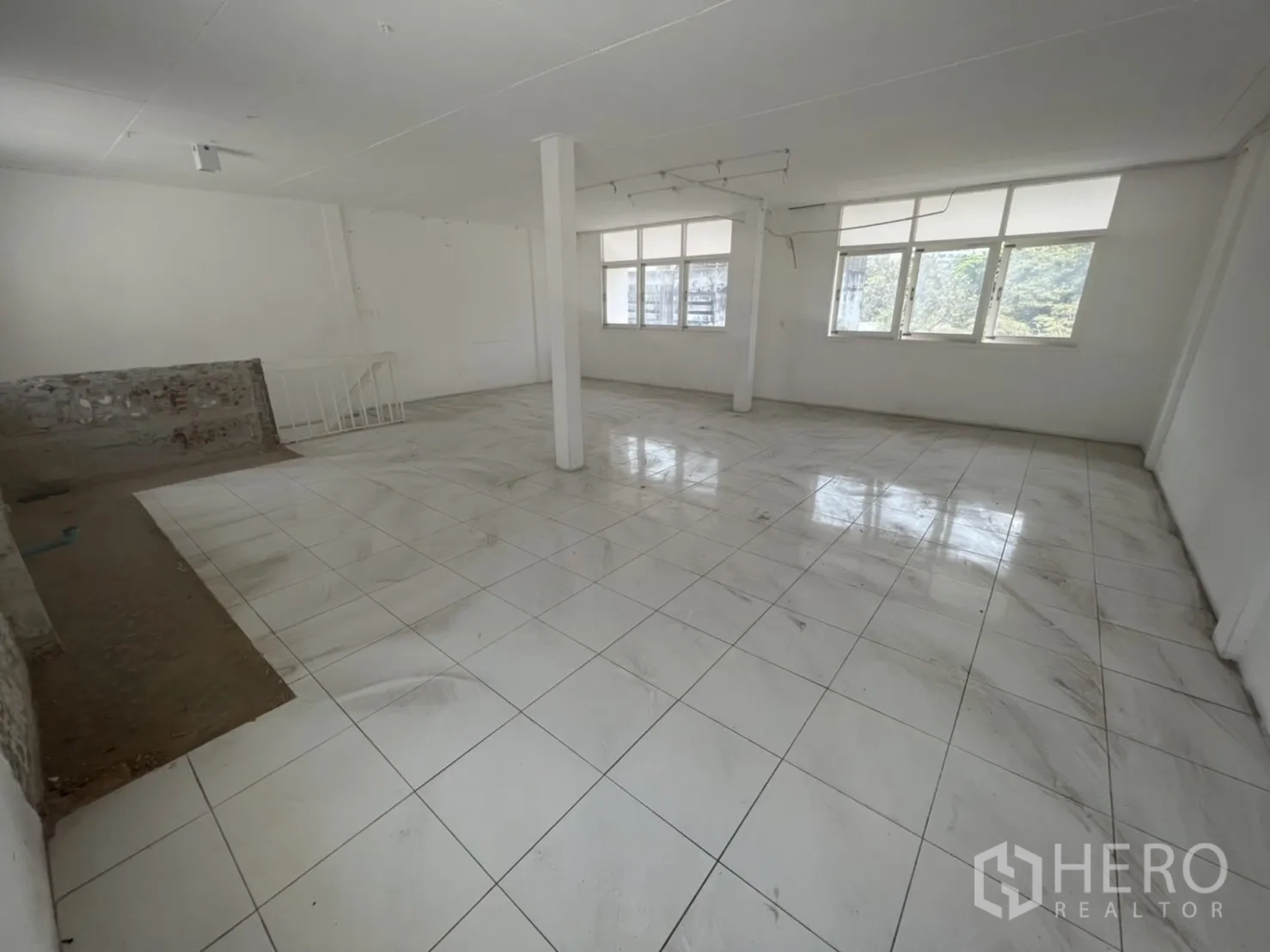 Shophouse for rent in Watthana, Bangkok - Large open room with glossy white tiles and a central column near windows.