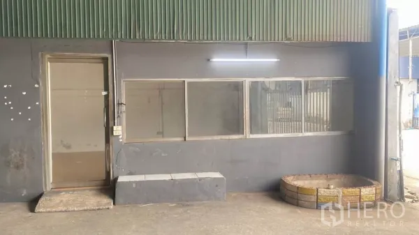 Factory for rent in Bang Sao Thong, Samut Prakan - Small office room with windows next to the warehouse entry under a corrugated canopy.