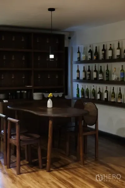 零售空间 for rent in Sathon, Bangkok - 私密用餐角落，圆形木桌、吊灯与陈列酒瓶和酒杯的层架。