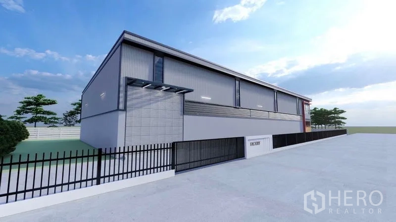 Warehouse for rent or sale in Lam Luk Ka, Pathum Thani - Modern grey warehouse exterior with roller shutter and black metal fence along a wide concrete drive.