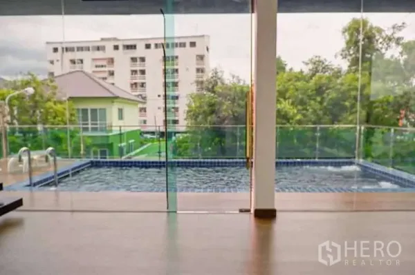 Detached House for sale in Lat Phrao, Bangkok - View through glass wall to a private pool with city apartment buildings beyond.