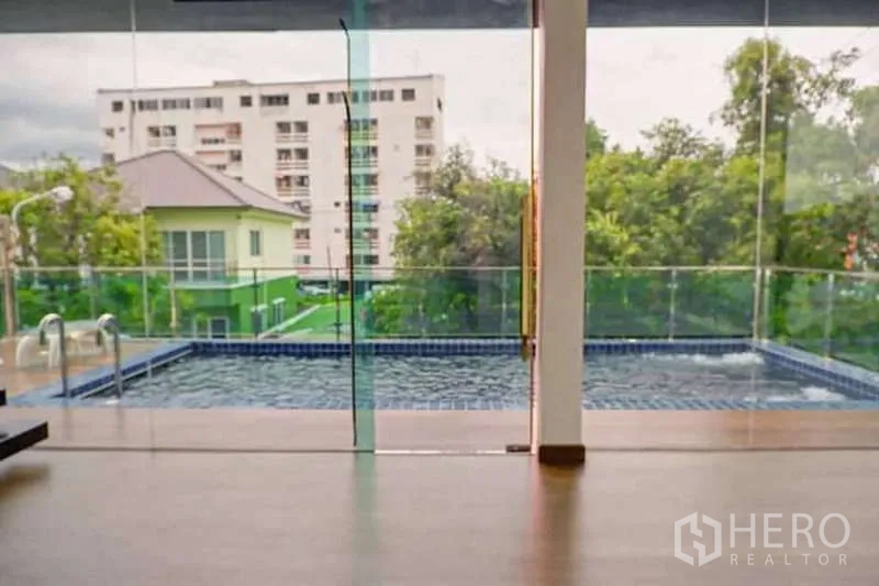 Detached House for sale in Lat Phrao, Bangkok - View through glass wall to a private pool with city apartment buildings beyond.