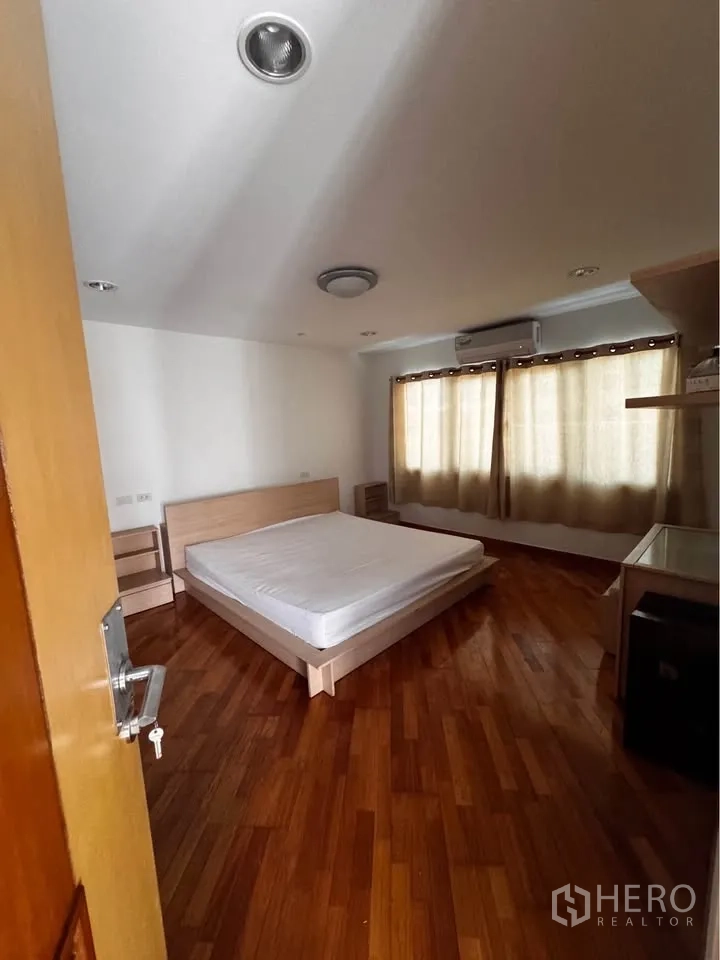 Townhouse for rent in Huai Khwang, Bangkok - Bedroom with light wood bed, side tables and curtains.