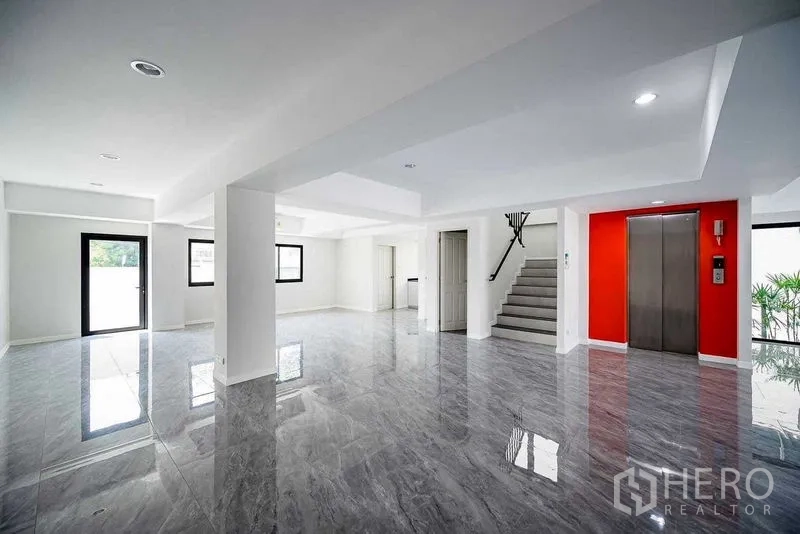 Home Office for rent in Suan Luang, Bangkok - Bright open-plan ground floor with glossy tiles, private elevator, and staircase with red accent wall.