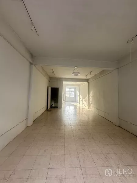 Shophouse for rent in Khlong Toei, Bangkok - Long empty retail floor with white tiles and window at the far end.