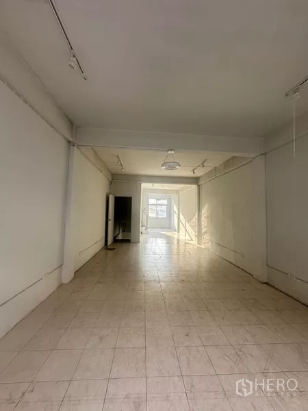 Shophouse for rent in Khlong Toei, Bangkok - Long empty retail floor with white tiles and window at the far end.