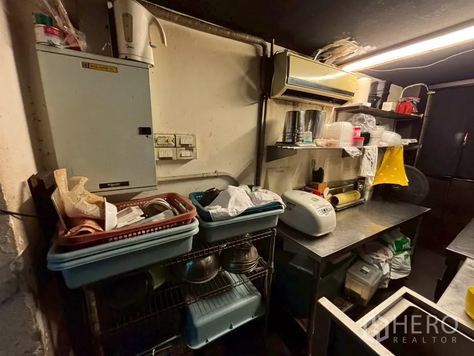 Shophouse for rent in Watthana, Bangkok - Pantry area with metal shelving, countertop workspace and air conditioner.