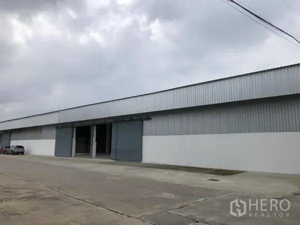 Warehouse for rent in Nonthaburi - Long side facade of the corrugated metal warehouse with multiple bays along an access road.