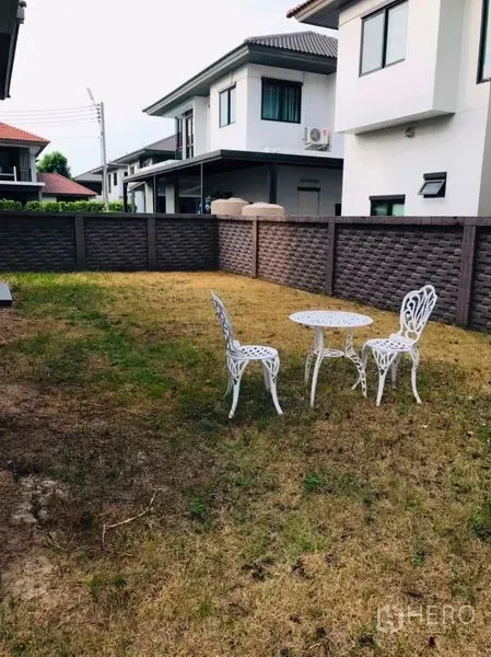 Detached House for rent or sale in Pathum Thani - Private fenced backyard lawn with white outdoor table and chairs.