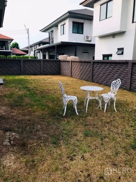 Detached House for rent or sale in Pathum Thani - Private fenced backyard lawn with white outdoor table and chairs.