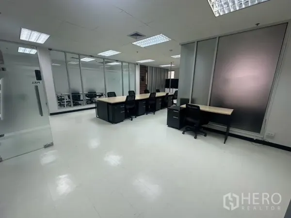 Office Space for rent - Workstation area featuring multiple desks, frosted glass panels, and a glass door entry.