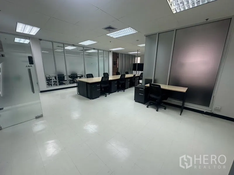 Office Space for rent - Workstation area featuring multiple desks, frosted glass panels, and a glass door entry.