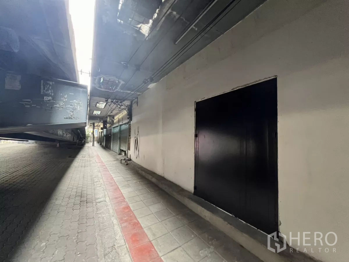 Shophouse for sale in Suan Luang, Bangkok - Black steel double door along a covered pedestrian passage beneath an elevated road.