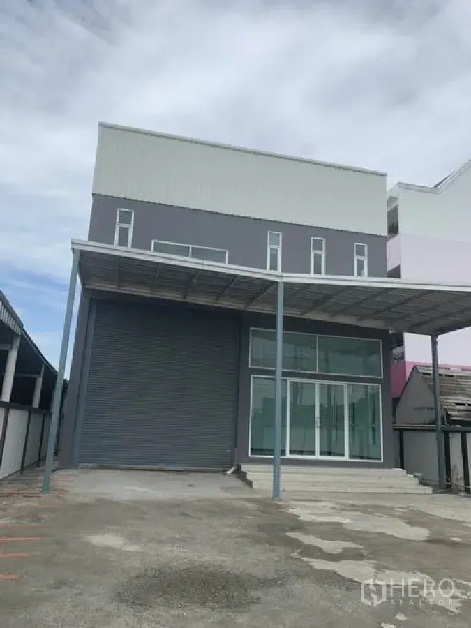 Warehouse for rent in Prawet, Bangkok - Modern two-storey warehouse exterior in Prawet, Bangkok featuring a tall roller shutter, glass-front office entrance and a covered loading area with a wide driveway.