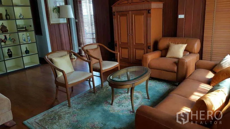 Townhouse for rent in Khlong Toei, Bangkok - Living room with leather sofa set, armchairs and display shelving.