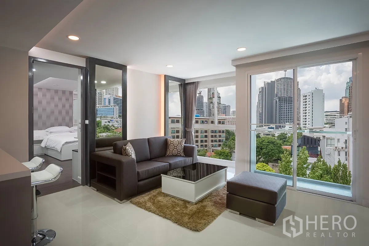 Condominium for rent in Khlong Toei, Bangkok - Living room with floor-to-ceiling windows showcasing a city skyline view beside the bedroom.
