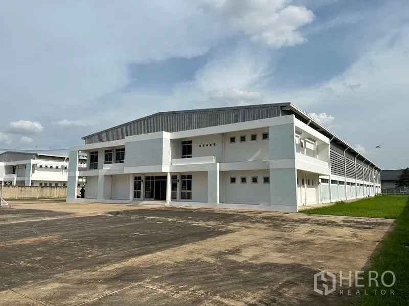 Factory for rent in Phra Nakhon Si Ayutthaya - Corner exterior of factory showing lawn edge and long ventilated side wall with metal cladding.