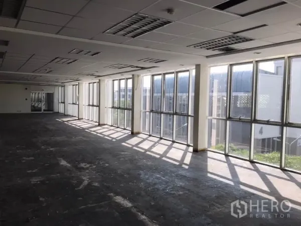 Office Space for rent in Khlong Toei, Bangkok - Corner office area with floor‑to‑ceiling windows bringing natural light over a concrete floor.