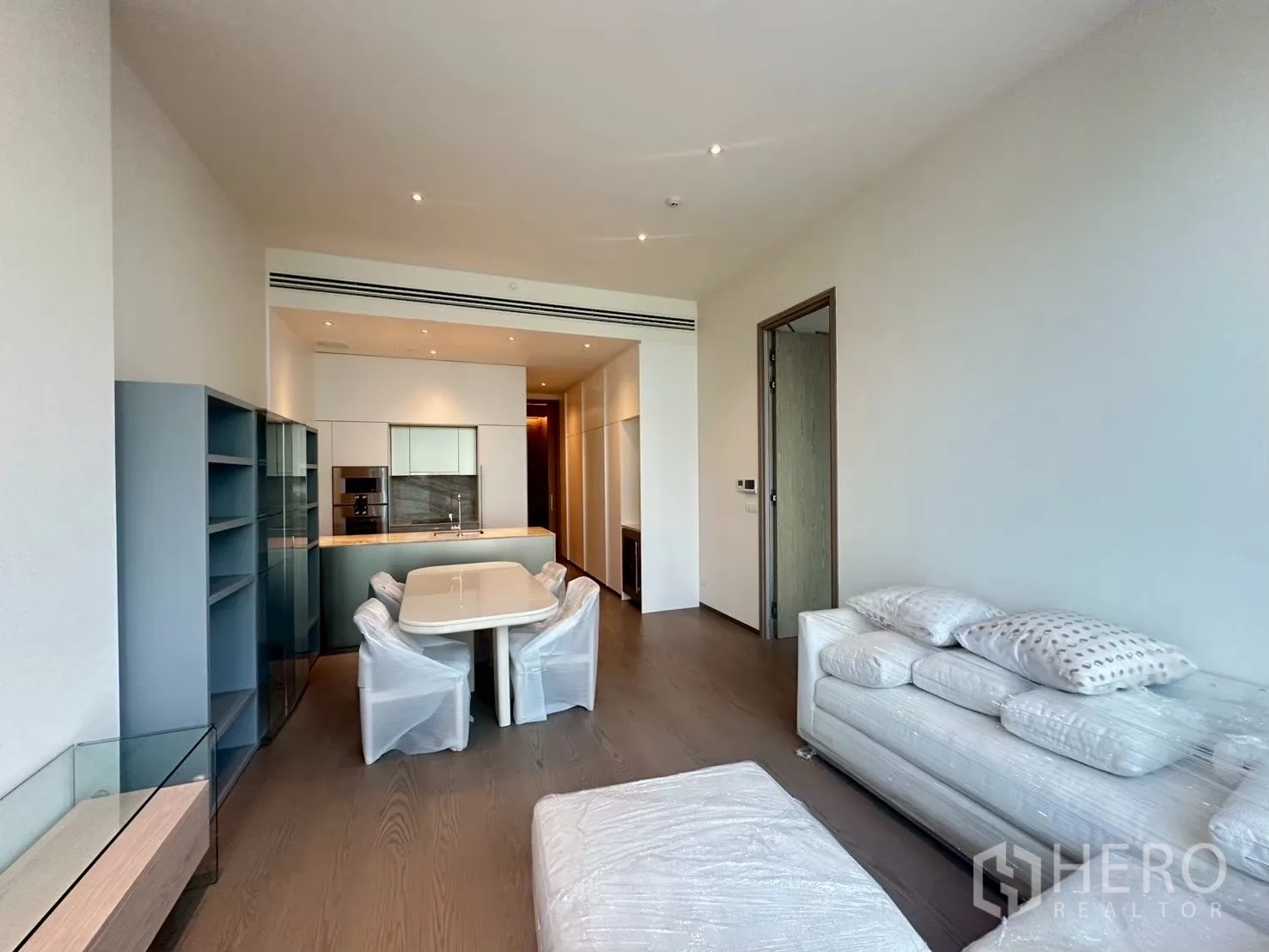 Condominium for rent in Pathum Wan, Bangkok - Open-plan living and dining area with modern kitchenette, built-in shelving, wood floors, dining table and a sofa.