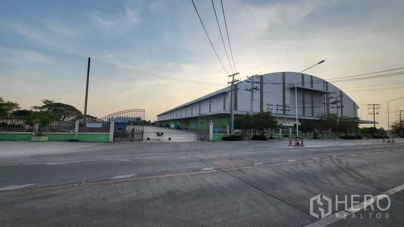 Factory for rent in Sai Noi, Nonthaburi - Corner exterior view of the factory complex with fenced entry and roadside power lines.