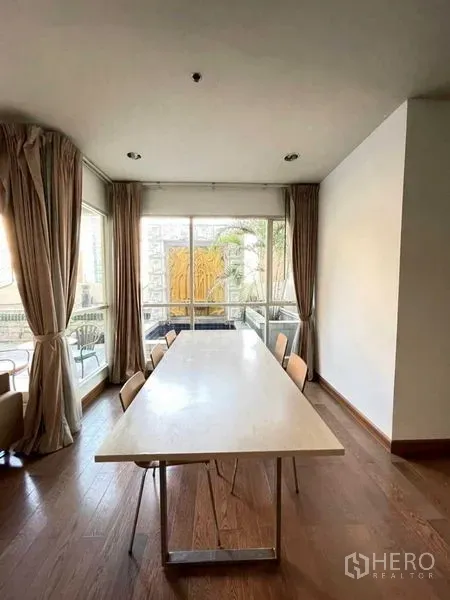 Condominium for rent in Pathum Wan, Bangkok - Bright dining area with long table, floor-to-ceiling windows and balcony in a Lumphini condo.