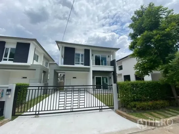 Detached House for rent in Khlong Luang, Pathum Thani - Front elevation of the home with wide driveway, lawn and tree-lined street.