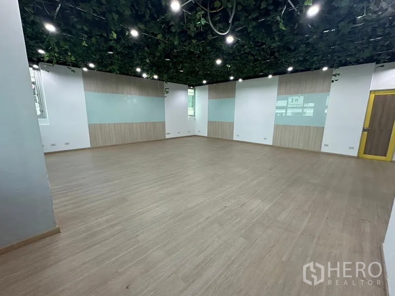 Office Space for rent in Ratchathewi, Bangkok - Large training room with wood-look floor and green ceiling vines and spotlights.