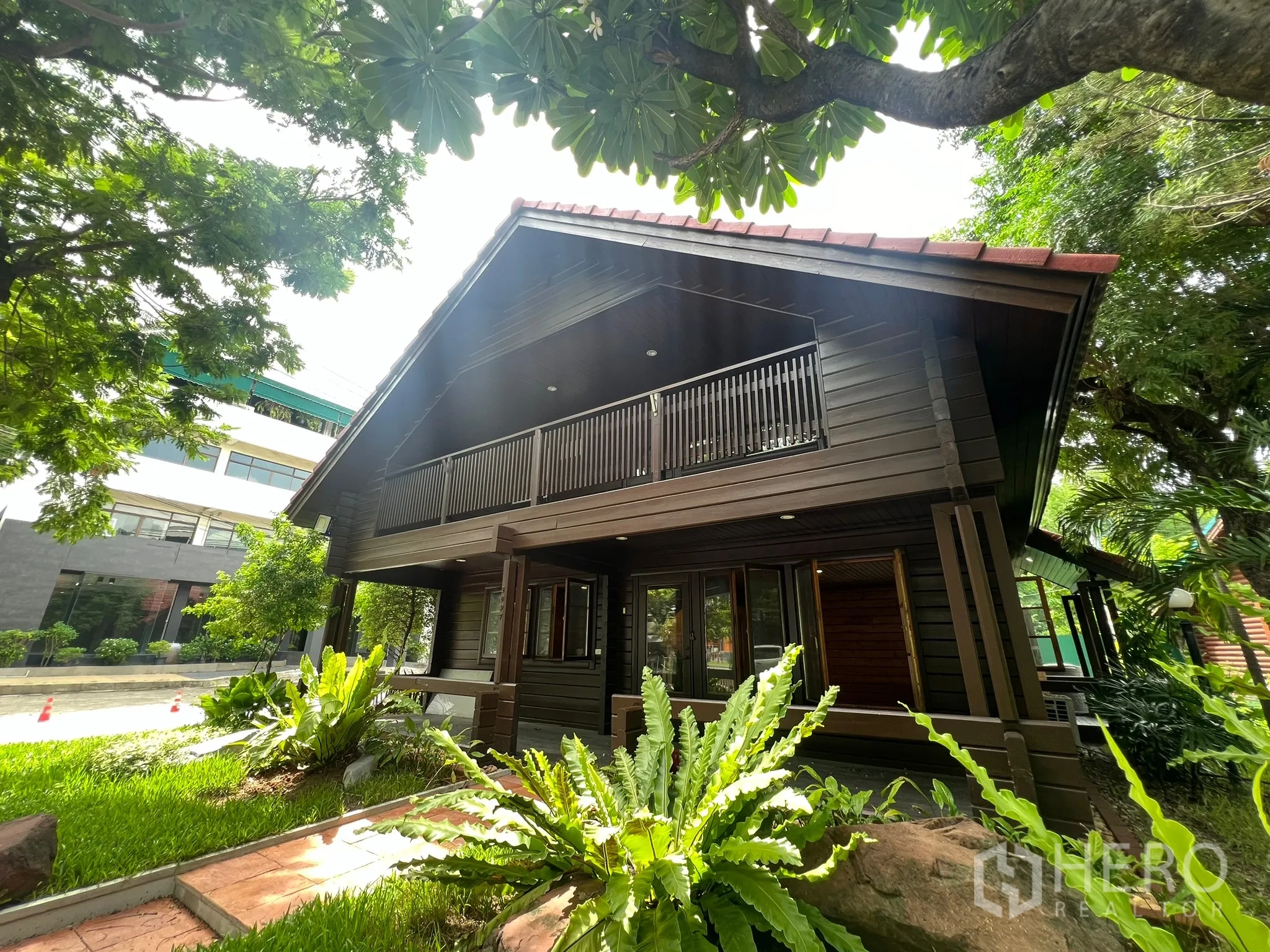 Home Office for rent in Suan Luang, Bangkok - Side exterior of wooden home office surrounded by lush greenery near a quiet street.