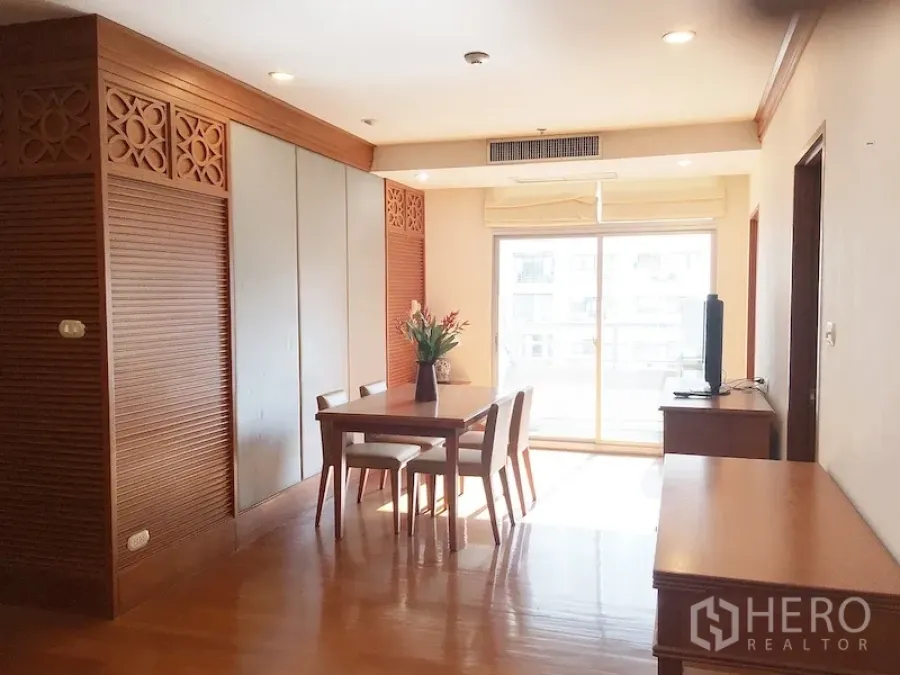 Condominium for rent in Pathum Wan, Bangkok - Bright dining and living space with wooden accents, dining table for four, TV console, and sliding glass door to a sunny balcony.