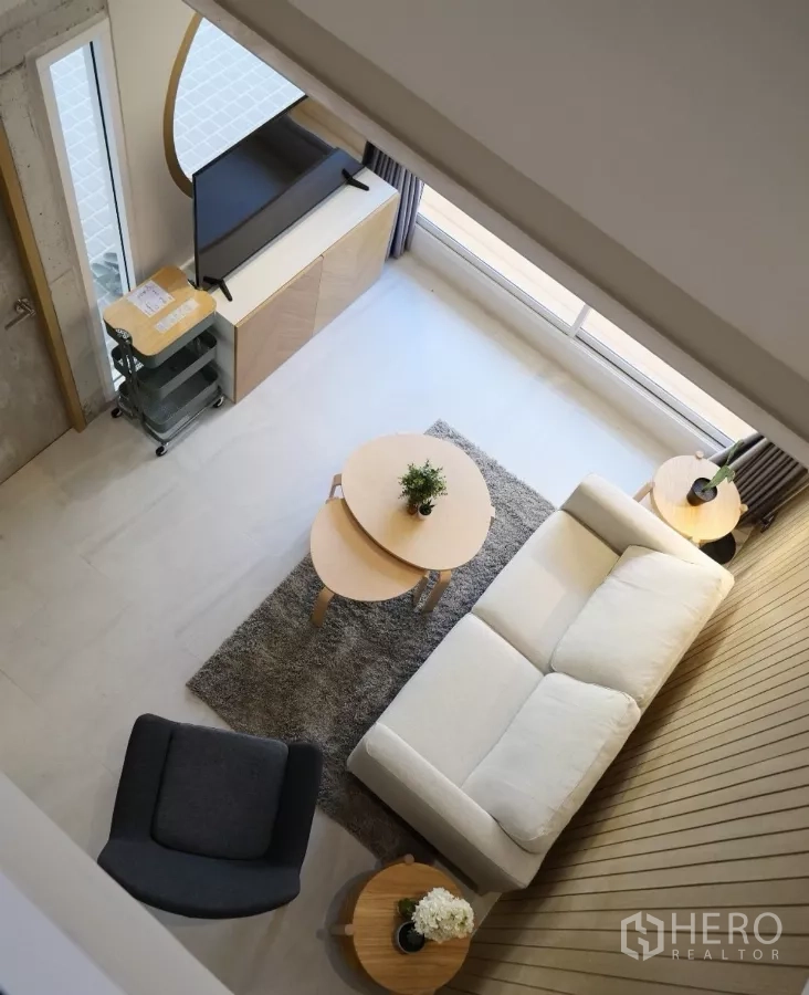 Townhouse for rent or sale in Watthana, Bangkok - Bird’s-eye view of the living room with sofa and nesting tables from the mezzanine.