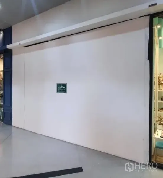 Retail Space for rent in Khlong Toei, Bangkok - Mall corridor frontage with a closed white shop entrance and small For Rent sign beside a neighboring display.