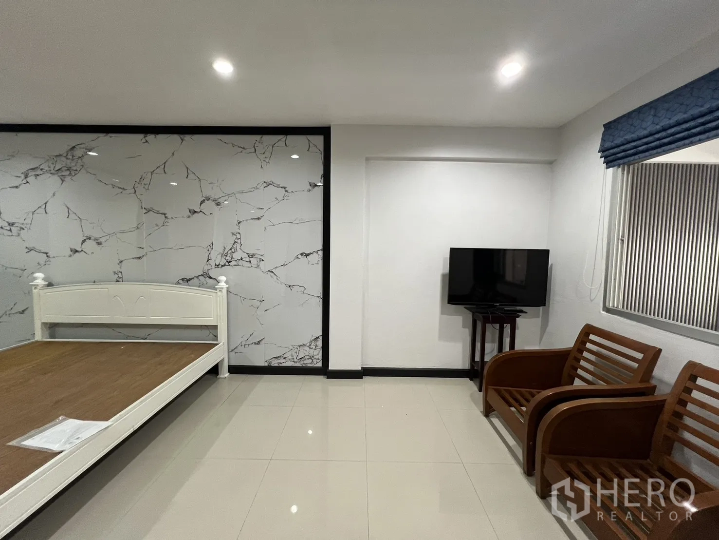 Townhouse for rent in Watthana, Bangkok - Bedroom corner with marble wall, TV and wooden lounge chairs.
