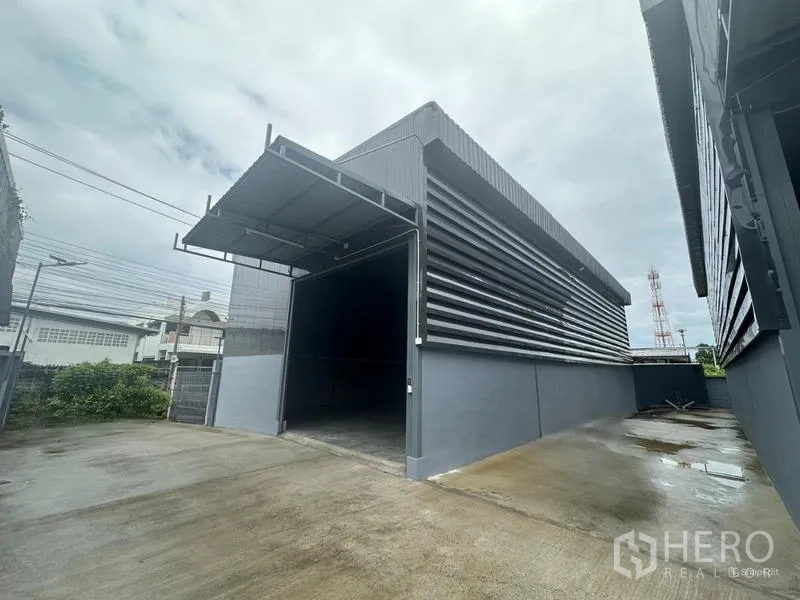 Warehouse for rent in Prawet, Bangkok - Modern gray warehouse exterior with covered loading bay and wide concrete driveway in Prawet, Bangkok.