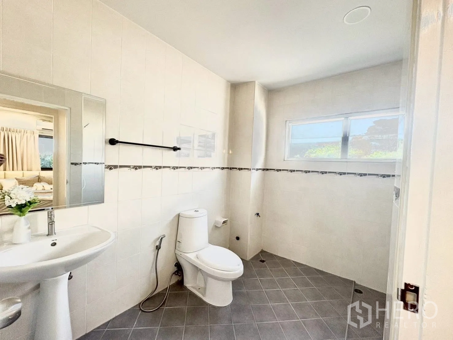 Townhouse for rent in Huai Khwang, Bangkok - Bright tiled bathroom with toilet, pedestal sink, mirror, and window.