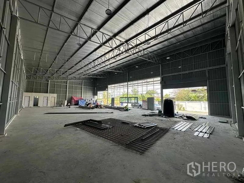 Warehouse for rent in Pak Kret, Nonthaburi - Open-plan storage area with full-height glazing, large roller doors and natural light across the concrete floor.