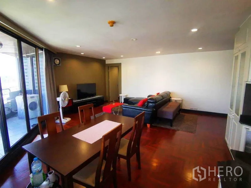 Condominium for rent in Khlong Toei, Bangkok - Open-plan living and dining room with leather sofa, TV and sliding doors to the balcony.