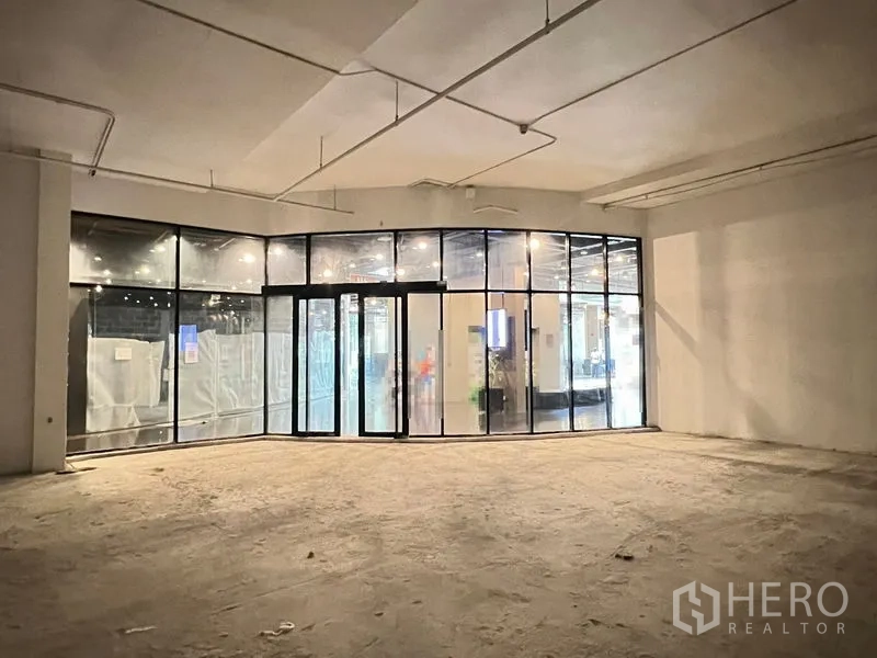 Retail Space for rent in Watthana, Bangkok - Empty 201 sqm retail unit with high ceiling and curved floor-to-ceiling glass storefront inside a mall.