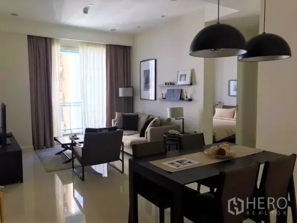 Condominium for rent in Pathum Wan, Bangkok - Open‑plan living and dining area with floor‑to‑ceiling windows, pendant lights and access to a bedroom.