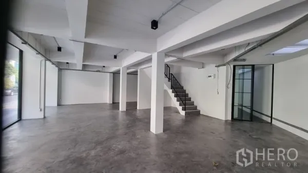Shophouse for rent in Khlong Toei, Bangkok - Spacious retail area featuring floor-to-ceiling windows and a staircase to upper levels.