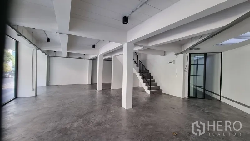 Shophouse for rent in Khlong Toei, Bangkok - Spacious retail area featuring floor-to-ceiling windows and a staircase to upper levels.