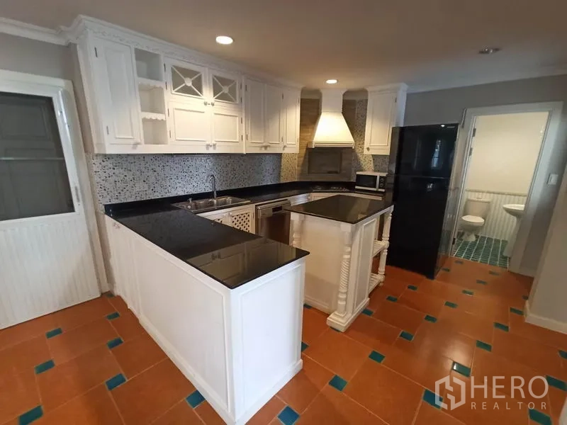 Detached House for rent in Mueang Samut Prakan, Samut Prakan - L-shaped kitchen with island, range hood, refrigerator and access to a guest bathroom.