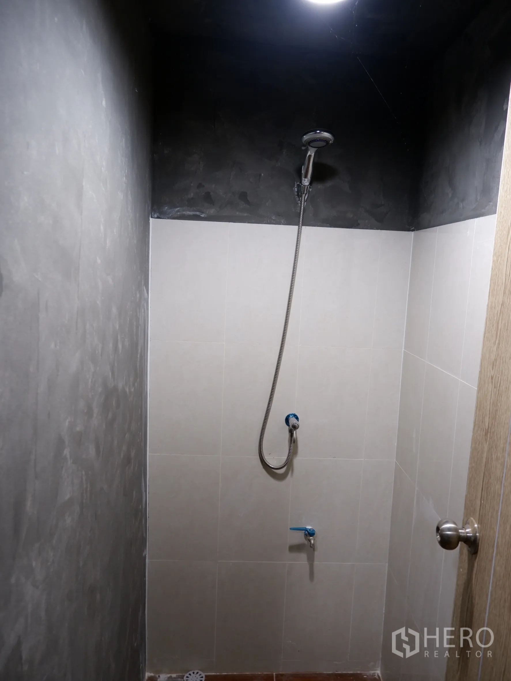 Home Office for sale in Bang Rak, Bangkok - Compact bathroom with a handheld shower and light gray wall tiles.