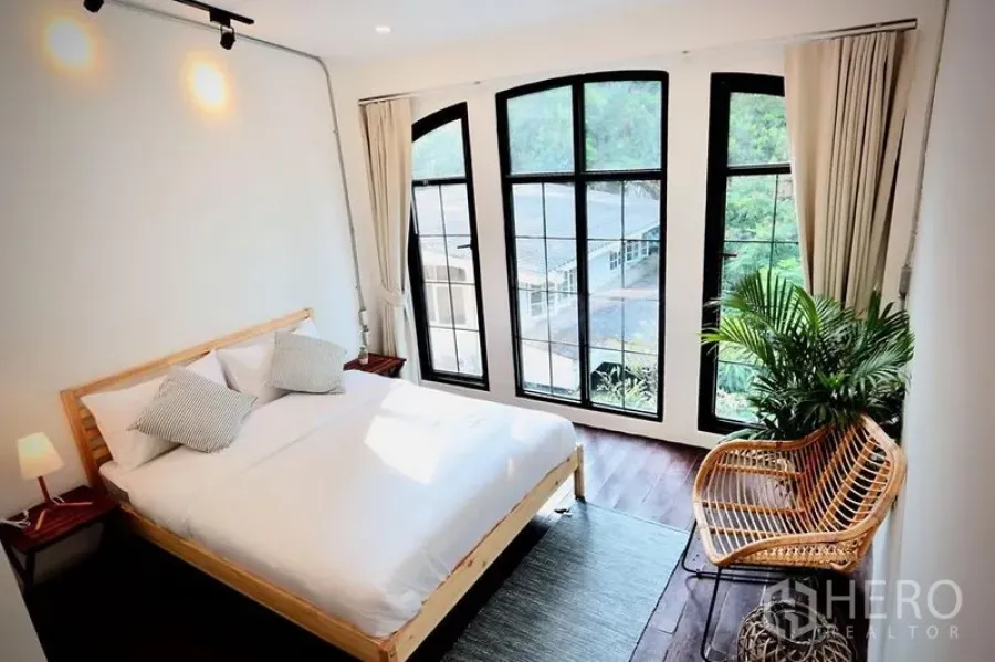 Townhouse for rent in Sathon, Bangkok - Bright bedroom with arched black-framed windows, wooden bed and rattan chair