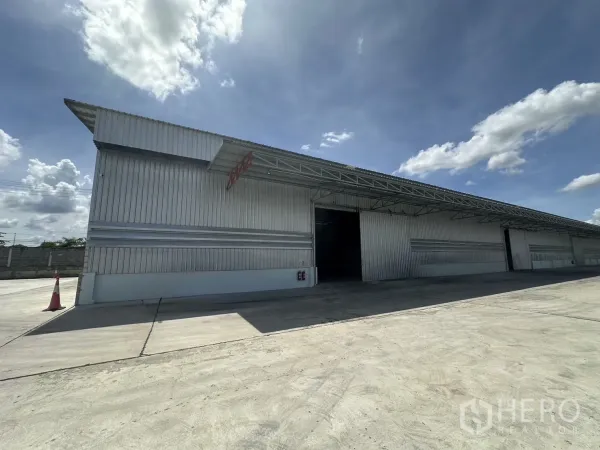 Warehouse for rent in Mueang Pathum Thani, Pathum Thani - Angled view of the long warehouse facade with canopy-covered loading areas and spacious truck-friendly driveway.