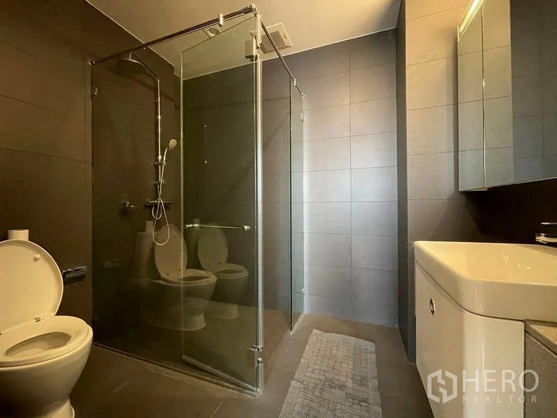 Condominium for rent in Pathum Wan, Bangkok - Modern bathroom with glass-enclosed shower, dark tiles and a sleek vanity.
