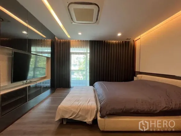 Detached House for sale - Master bedroom with king bed, built-in TV wall, dark curtains and ceiling cassette AC in a detached house in Bang Phli, Samut Prakan.