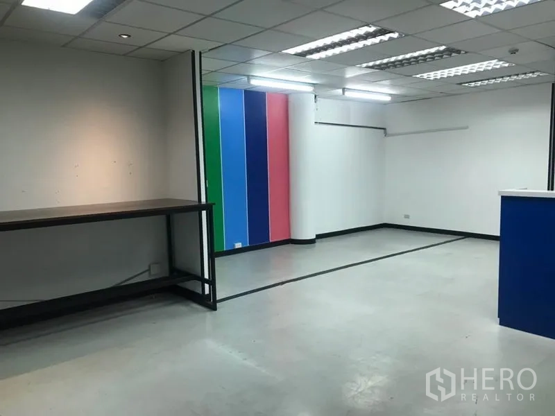 Office Space for rent in Khlong Toei, Bangkok - Open-plan office with a colorful feature wall, built-in workbench, and bright fluorescent lighting.