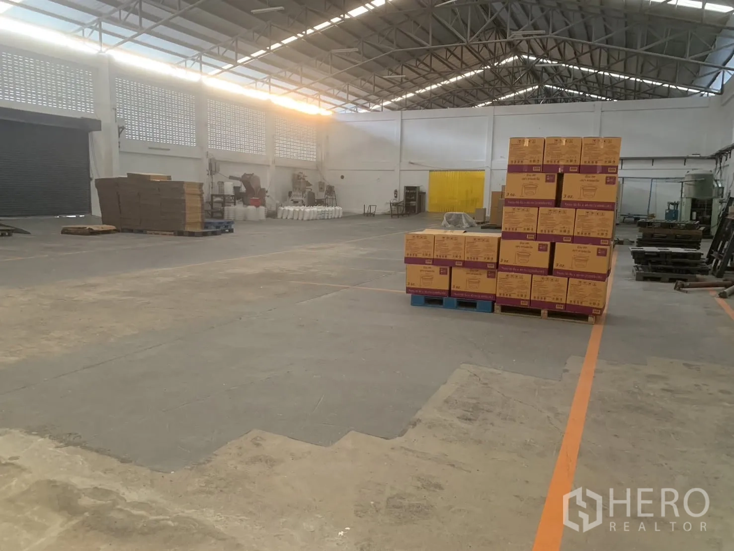 Warehouse for rent in Bang Phli, Samut Prakan - Spacious warehouse interior with steel truss roof, stacked cartons on pallets, and marked floor lanes.