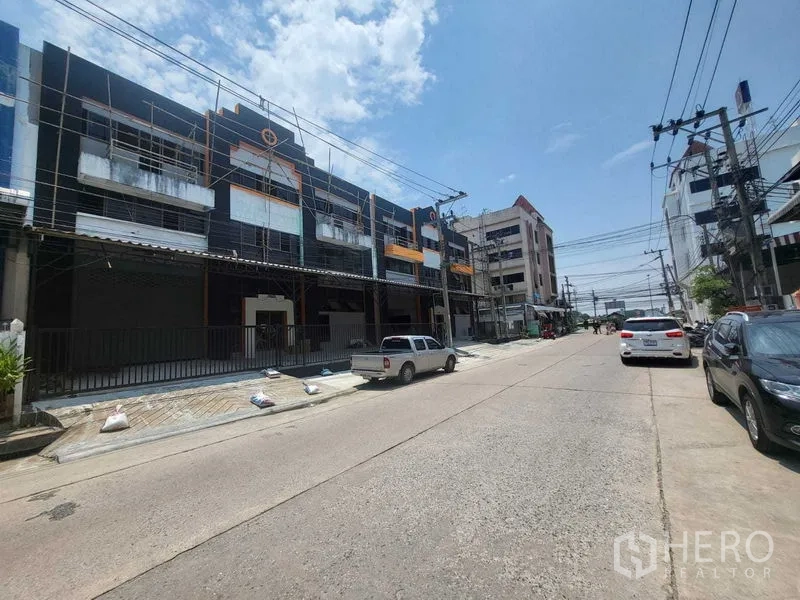Factory for rent or sale in Samut Prakan - Street view of the property frontage with parking and nearby commercial buildings.